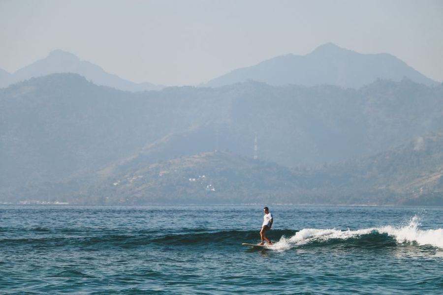 Surfer on a wave with hills behind, Lombok